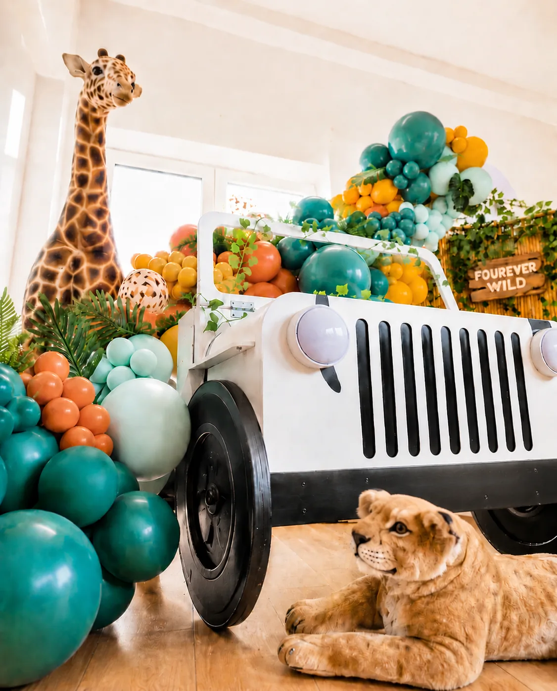 White safari jeep prop with teal and orange balloon garland, a giraffe and a lion cub at a jungle children's party in Surrey